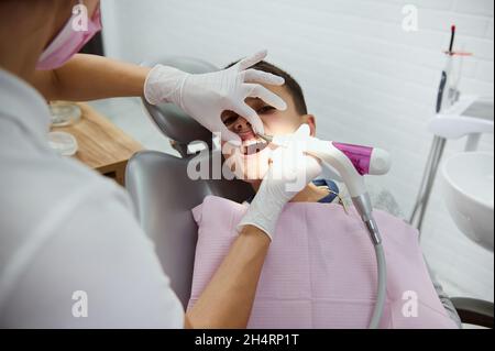 Adorabile bel ragazzo di età elementare seduto in sedia dentista durante la visita pediatrica dentista in clinica dentale bianca moderna, ricevendo orale medico Foto Stock