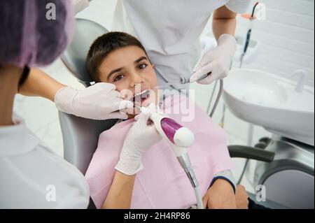 Ragazzo coraggioso della scuola nella sedia del dentista durante un check-up dentale, ricevendo il trattamento dei denti alla clinica di dentista dei bambini. Concetto di diagnosi precoce Foto Stock