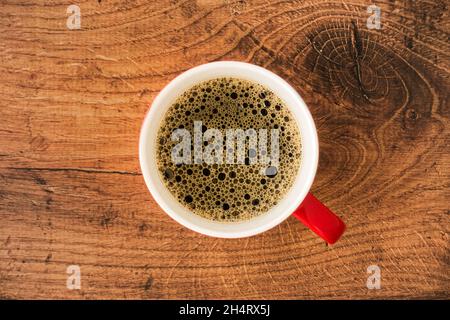 Vista dall'alto di una tazza rossa riempita di caffè nero su sfondo marrone scuro rustico di legno di quercia con molto spazio per la copia. Foto Stock