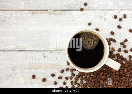 Vista dall'alto di una tazza, una tazza di caffè nero e chicchi di caffè torrefatto su legno bianco rustico resistente agli agenti atmosferici con molto spazio per la copia. Foto Stock