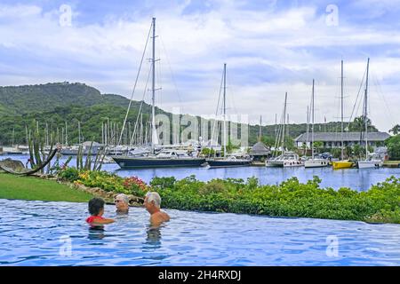 Barche a vela e yacht ormeggiati nel porto inglese e turisti occidentali in piscina sull'isola Antigua, piccole Antille nel Mar dei Caraibi Foto Stock