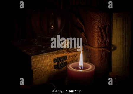 Immagine di un dado metallico a 20 lati per giocare di ruolo su una scatola di legno accanto a una sfera di cristallo e vecchi libri illuminati da lume di candela Foto Stock