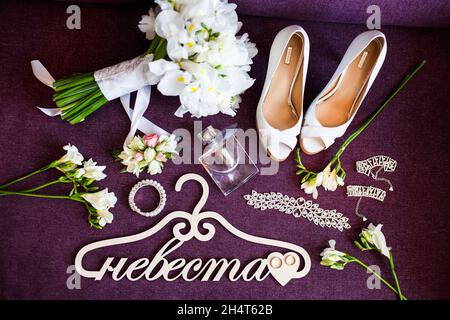 Tipico set da sposa: Scarpe, bouquet di iridi, appendiabiti con iscrizione 'sposa' in lingua russa, gioielli e profumi. Foto Stock