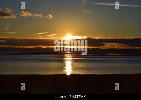 Il sole tramonta verso il basso rivelando riflessi d'acqua scintillanti e nuvole scure sopra l'estuario del fiume Mersey. Foto Stock