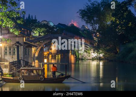 Un tour in barca passa di fronte al ponte Renji sul fiume Xishi in serata a Wuzhen, Cina. Foto Stock
