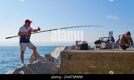 brixham, devon. Maggio 31, 2021. L'uomo con una maschera medica sul viso ha dato un pollice fino a sua moglie a causa della pesca riuscita, sua moglie ha preso th Foto Stock