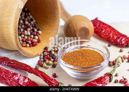 Peppercorn secco mescolare nel mortaio con pestello, peperoncino secco in polvere per cucinare su fondo di legno chiaro tagliere in cucina. Foto Stock