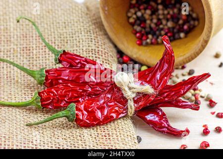 Mescolare i grani di pepe secco nel mortaio di legno e il peperoncino secco per cucinare su sfondo chiaro in cucina. Foto Stock