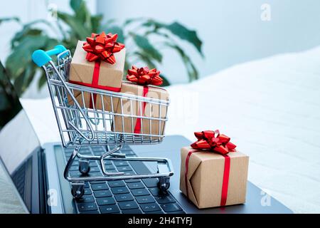 Il concetto di shopping online. Computer portatile e piccolo carrello. Vendite natalizie. Consegna rapida. Regali al momento dell'ordine Foto Stock