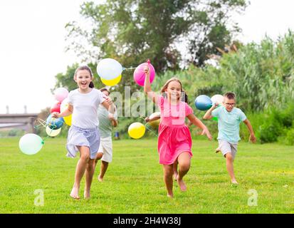 Allegri tweenagers con palloncini colorati in mano che corrono nel parco estivo Foto Stock