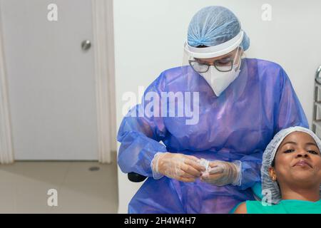 Una bella donna afroamericana seduta nella sedia del dentista. Una dentista femminile che controlla i denti in un esame dentale. Foto Stock