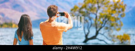 Viaggi lifestyle persone turisti fotografare con telefono su New Zealand Wanaka tree background Coppia vacanza banner panorama. Foto Stock