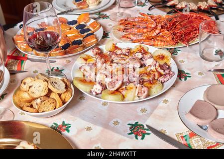 Varietà di antipasti al tavolo preparati per la cena di Natale con tartine di salmone e caviale, un piatto di polpo galiziano, gamberi alla griglia Foto Stock