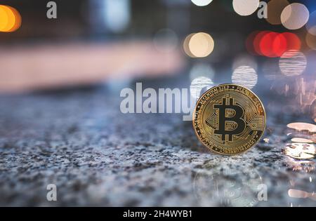 Moneta criptata Bitcoin con spazio copia, in piedi all'aperto con sfocato bokeh notte luci di sfondo città e riflessione su superficie bagnata. Banner token di criptovaluta BTC singolo, messa a fuoco morbida Foto Stock