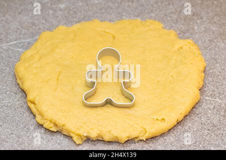 Forma per tagliare gli uomini di pan di zenzero su pasta grezza arrotolata su sfondo grigio. Il processo di fare i biscotti di Natale nel paese. Tradizione culinaria di Natale Foto Stock