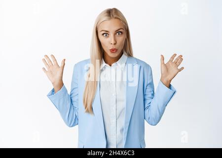 Immagine di donna di affari sorpresa goccia qualcosa, sollevando mani vuote in su e guardando stordled, vestito, in piedi su sfondo bianco Foto Stock