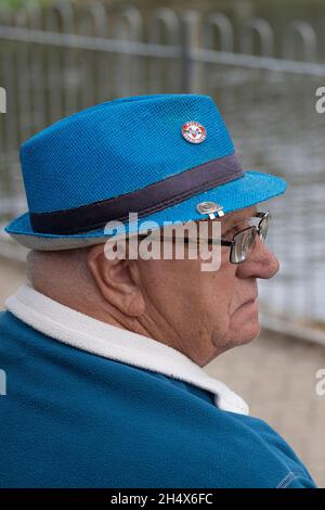 Uomo maturo che indossa un pile blu e un cappello blu con un distintivo completamente vaccinato. Foto Stock