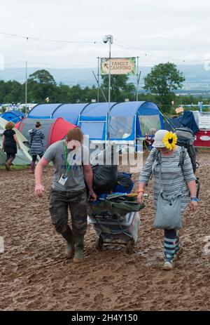 Festival Goers portando le loro attrezzature da campeggio attraverso il fango al Kendal Calling Festival a Lowther Deer Park il 08 agosto 2015 a Kendal, Regno Unito Foto Stock