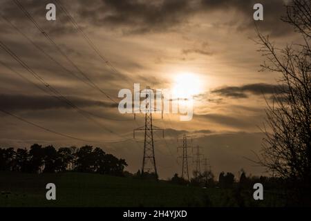 Linee elettriche aeree ad alta tensione e tralicci che trasportano energia elettrica attraverso la campagna britannica ambientando il cielo del tramonto invernale. Foto Stock