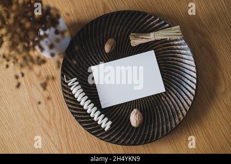 Carta bianca mockup carta su piatto con decorazioni autunnali e vaso di lino essiccato su tavola di legno vista dall'alto. Higge, arredamento accogliente soggiorno casa. Piatto l Foto Stock