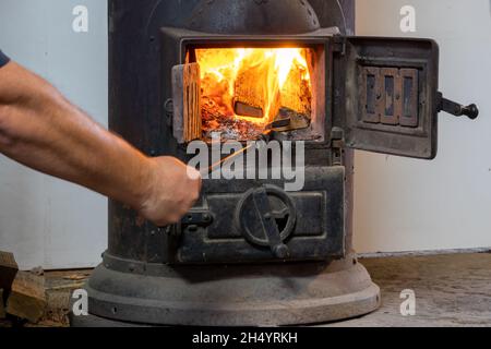 Uomo che mette il ceppo a legna bruciando stufa Foto Stock