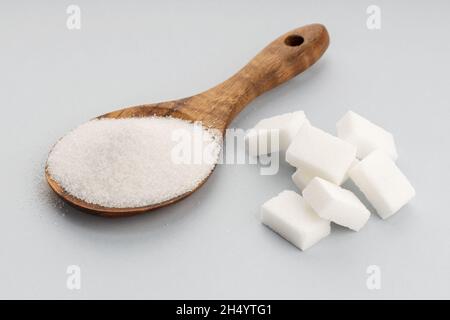 Zucchero in cucchiaino di legno e cubetti di zucchero su sfondo grigio. Primo piano Foto Stock