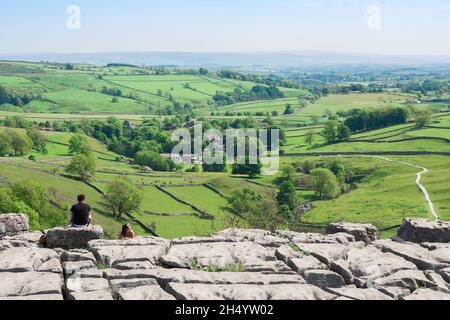 Malham Cove, vista in estate delle persone seduti vicino al bordo della scogliera del marciapiede calcareo a Malham Cove e guardando lo Yorkshire Dales, Inghilterra Foto Stock