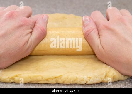 Le mani dello chef stendere l'impasto con un mattarello su un tavolo grigio, primo piano. Pasta da cucina per torta, pizza, biscotti. Concetto di cottura domestico Foto Stock