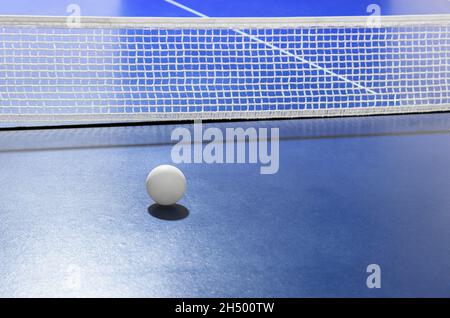 Primo piano di ping-pong palla di fronte alla rete sul tavolo blu come sfondo sportivo Foto Stock