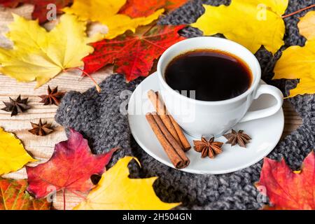 Accogliente mattinata autunnale con tazza di caffè con cannella, anice stellato, maglione accogliente e foglie autunnali su sfondo di legno. Caffè caldo con spezie sul o Foto Stock
