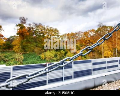 primo piano di una catena di fronte ad una barriera insonorizzata contro gli alberi Foto Stock