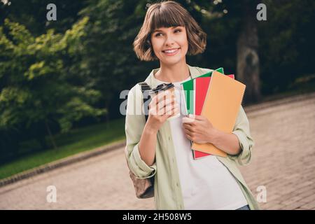 Ritratto di attraente ragazza allegra bere latte bevanda tenendo copybook educativo su aria fresca all'aperto Foto Stock