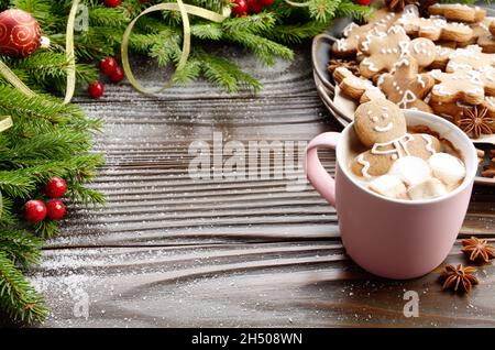 Rosa la tazza con il cioccolato caldo marshmallows e gingerbread man sullo sfondo del ramo di abete e il vassoio con i cookie Foto Stock