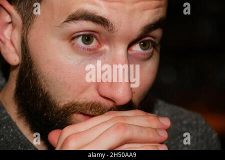 L'uomo in bearded bianco siede in un ristorante di notte con le espressioni facciali differenti. Foto Stock