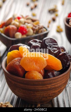 Datteri secchi e albicocche in ciotola di argilla su cucina di legno primo piano del tavolo Foto Stock