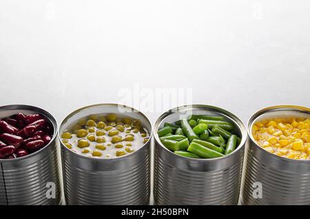 Fagioli, fagioli verdi, piselli e mais in lattine aperte su tavola da cucina. Fondo di alimenti non deperibili Foto Stock