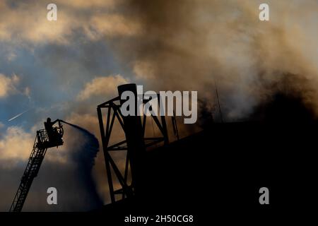 Hannover, Germania. 05 novembre 2021. I vigili del fuoco spengono il fuoco di un locale industriale a Brinker Hafen da una scala giradischi alla luce del sole che tramonta. Credit: Moritz Frankenberg/dpa/Alamy Live News Foto Stock