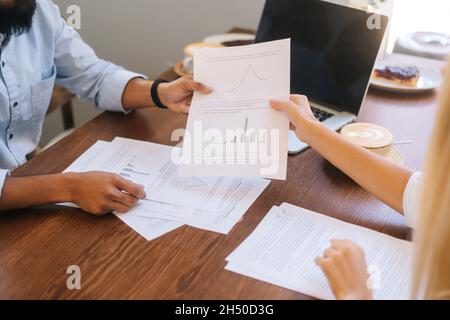 Primo piano di due colleghi discutono i dati finanziari in un report utilizzando documenti cartacei e grafici seduti alla scrivania in un accogliente bar. Foto Stock