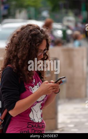 Timisoara, Romania - 01 giugno 2016: Ragazza che controlla il suo telefono mentre cammina per la strada. Persone reali. Foto Stock