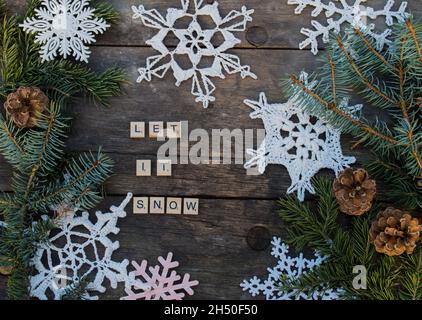 ornamenti in fiocco di neve a crochet su terreno di legno con slogan invernali e ramo di abete e coni sfondo di lettere in legno Foto Stock