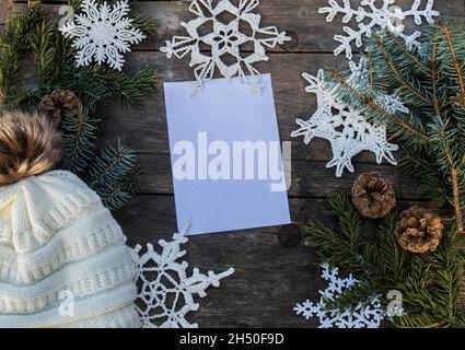 ornamenti in fiocco di neve a crochet su terreno di legno con spazio per il testo e ramo di abete e coni e un cappello di bobble lavorato a maglia fondo Foto Stock