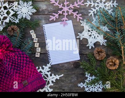 ornamenti in fiocco di neve a crochet su terreno di legno con spazio per il testo e ramo di abete e coni e un cappello di bobble lavorato a maglia fondo Foto Stock