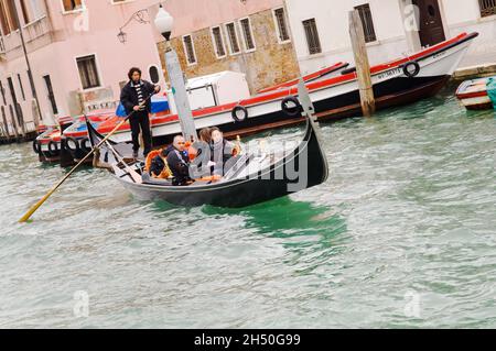 Un gondoliere lo sterzo una gondola tra le altre barche tra cui il fiume fermata autobus a venezia, Italia, vicino alla stazione ferroviaria. Foto Stock