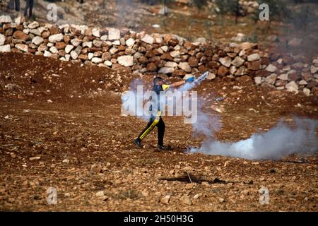 Riva occidentale, Nablus, Palestina. 5 novembre 2021. Un dimostratore palestinese lancia barattoli di gas lacrimogeni ai soldati israeliani durante una dimostrazione contro gli insediamenti israeliani nel villaggio di Beit Dajan vicino alla città di Nablus in Cisgiordania. Credit: Nasser Ishtayeh/ZUMA Wire/Alamy Live News Foto Stock