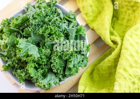 Vista dall'alto del cavolo fresco verde riccio o delle foglie di insalata di cavolo tagliate nel recipiente su sfondo chiaro sul tavolo in cucina. Foto Stock