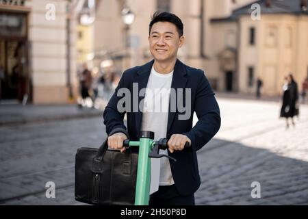 Uomo d'affari asiatico che guida scooter elettrico in città Foto Stock