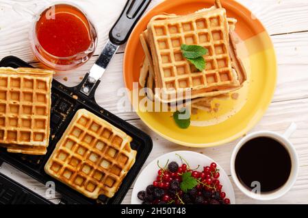 Vista piatta sulle cialde belghe sulla padella colata e. accatastato su un piatto con sciroppo di bacche e caffè da parte Foto Stock