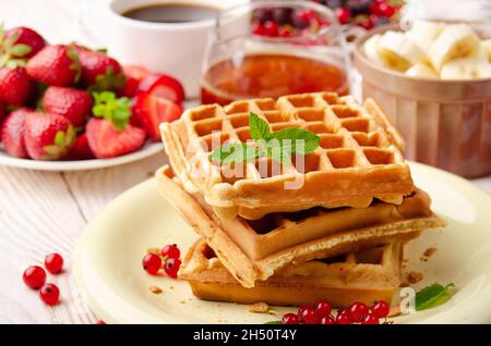 Pila di tre cialde belghe su tavolo da cucina bianco con fragole banane sciroppo caffè e ribes rosso Foto Stock