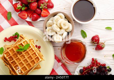 Vista su tre cialde belghe su una cucina bianca tavolo con fragole, sciroppo di banane, caffè e ribes rosso Foto Stock