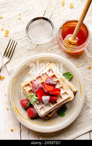 Vista piatta sui waffle belgi serviti con fragole e. foglie di menta spolverate con zucchero in polvere Foto Stock